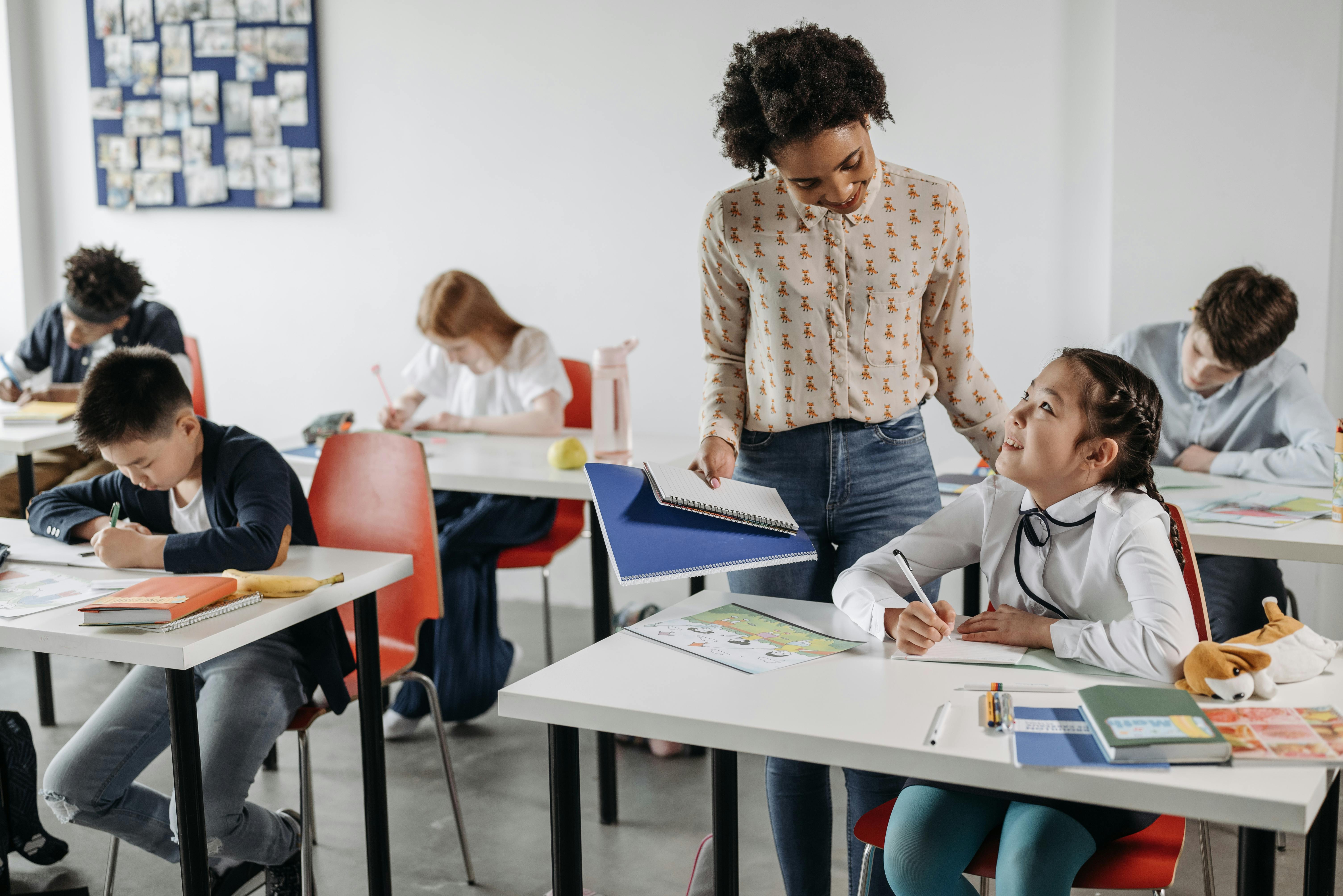 A classroom full of students with a teacher helping one of the students